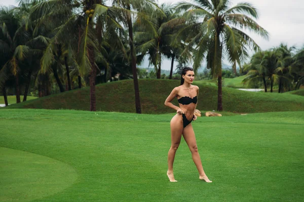 Giovane sexy e bella ragazza bruna fitness in costume da bagno nero posa svolta bottino mostra culo all'erba verde del Golf club. Modello sexy ritratto con corpo perfetto. Concetto di vacanza estiva — Foto Stock