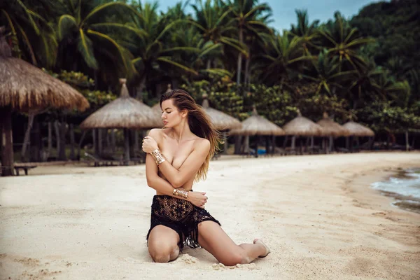 Портрет сексуальної жінки в чорному бікіні, без бюстгальтера. Молода красива дівчина з відмінною фігурою позує на пляжі, сидячи на піску. Концепція подорожей і способу життя — стокове фото