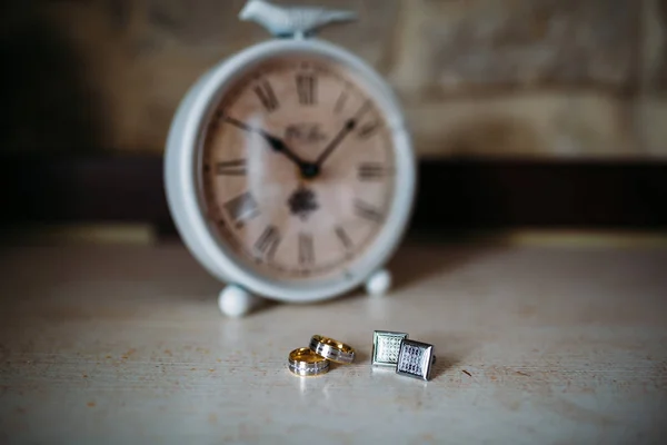 Wedding accessories. Gold rings and cufflinks on white textured table and clock on the background