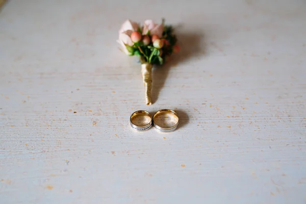 Bruiloft accessoires. Corsages, gouden ringen, een mooi boeket bloemen op witte getextureerde tafel. Concept van bruid en bruidegom versieringen — Stockfoto
