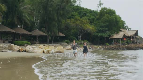 Jovem casal apaixonado correndo na praia do mar de mãos dadas, sorrindo e rindo em câmera lenta. O conceito de uma família feliz e descanso — Vídeo de Stock