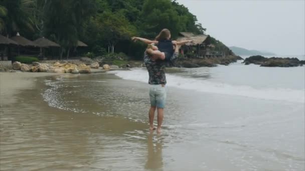 Homem está girando uma mulher em seus ombros, um jovem casal apaixonado rodopiando em uma praia do mar. O conceito de uma família feliz e descanso — Vídeo de Stock