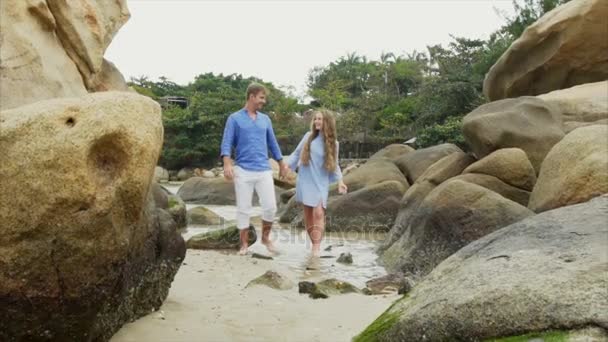 Lento movimiento joven feliz hermosa pareja de amantes, en ropa azul, tomados de la mano, caminando a lo largo de la orilla del mar, hablando y sonriendo. concepto de una fecha de luna de miel y familia de la felicidad — Vídeo de stock