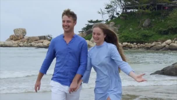 Мужчина держит девушку за руку. Они ходят по пляжу, разговаривают и улыбаются — стоковое видео
