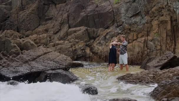 La chica baila en la orilla del océano y sostiene al hombre de la mano, en cámara lenta. Hermosa vista de la playa de mar con olas — Vídeos de Stock