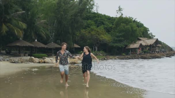 Giovane coppia innamorata che corre sulla spiaggia del mare tenendosi per mano, sorridendo e ridendo al rallentatore. Il concetto di una famiglia felice e di riposo — Video Stock