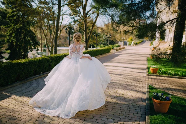 Uma noiva bonita com cabelo loiro correndo acenando seu vestido em um dia de casamento. vista para trás — Fotografia de Stock