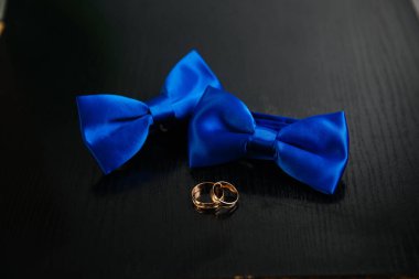 İki mavi papyon ve siyah arka plan üzerine altın alyans. Giysi kavramı