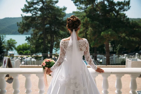 Vackra brud i en lyxig vit klänning, bakifrån. Sjön och bergen i bakgrunden — Stockfoto