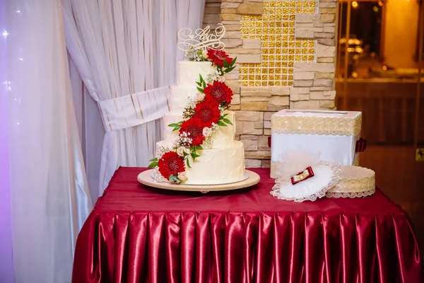 Weiße mehrstöckige Hochzeitstorte mit roten Cremeblüten auf dem Tisch. Schokoriegel-Konzept — Stockfoto