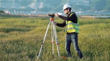 İş elbiseleri içinde erkek bir surveyor ekipman inşaat alanı üzerinde ayarlar. Peyzaj konsept tasarımı, Jeodezi