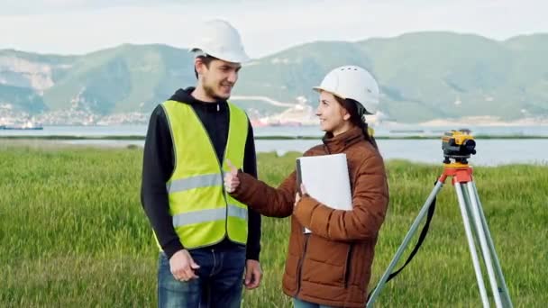 男、女测量员在工作服和头盔上微笑着表示竖起大拇指, 这意味着良好的工作。景观设计的概念, 大地测量学 — 图库视频影像