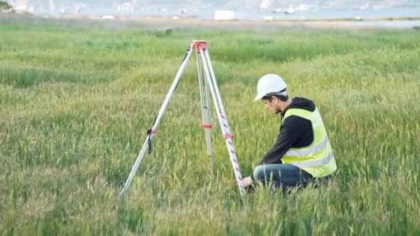 Egy férfi földmérő munkaruha beállítja a berendezés az építkezésen. A koncepció a táj design, Geodézia — Stock videók
