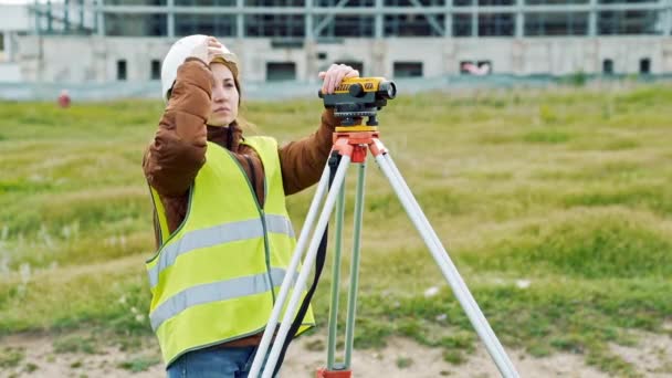 Een jonge vrouw landmeter in werkkleding en helm past de apparatuur en produceert berekeningen op de bouwplaats. Het concept van landschap design, geodesie — Stockvideo