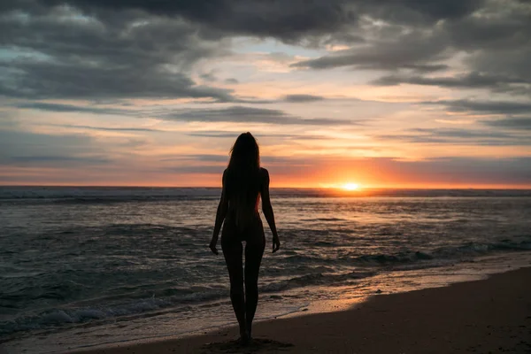 Back view silhouette of sexual woman. Beautiful young girl with long hair walking on the beach, posing at sunset. Concept of travel, relax, yoga — Stock Photo, Image