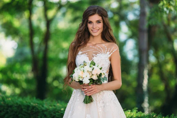 Noiva incrível em vestido de noiva branco bonito segurar buquê de flores em suas mãos. Conceito de roupa e florística — Fotografia de Stock