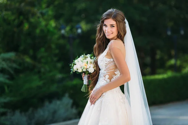 Die wunderbare Braut im wunderschönen weißen Brautkleid hält einen Blumenstrauß in ihren Händen. Konzept der Kleidung und Floristik — Stockfoto
