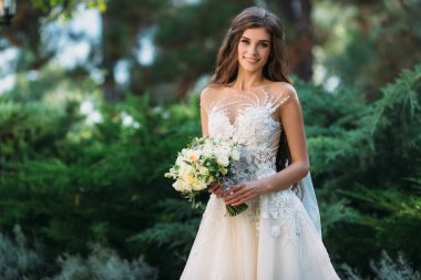 Güzel gelin güzel kokulu çiçek elinde. Düğün makyajlı yeşil çim zemin üzerine beyaz elbiseli çekici genç kadın. Portre gülümseyen gelin kapatın