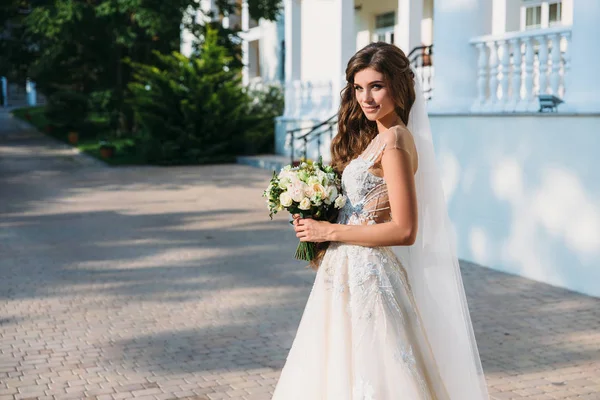 Porträt der schönen jungen Braut mit süßem Schlag im weißen Hochzeitskleid hält Blumenstrauß in ihren Händen. Konzept von Kleidung und Familie — Stockfoto