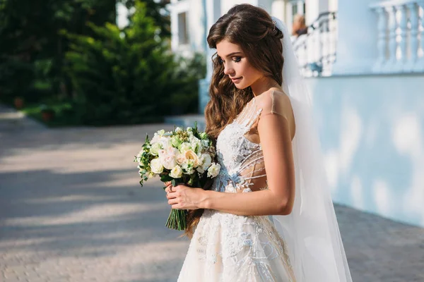 Porträtt av vackra unga bruden med söt smite i vit bröllop klänning håll bukett blommor i hennes händer. Begreppet kläder och familj — Stockfoto