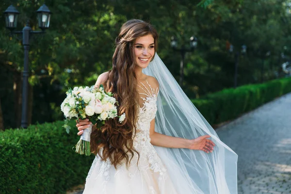 Hübsche Braut mit schönem Blumenstrauß in den Händen. attraktive junge Frau im weißen Kleid mit Hochzeitsschminke auf grünem Gras-Hintergrund. Nahaufnahme Porträt lächelnde Braut — Stockfoto