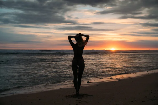 Rückseite Silhouette der sexuellen Frau. schönes junges Mädchen mit langen Haaren, das am Strand spaziert und bei Sonnenuntergang posiert. Konzept des Reisens, der Entspannung, des Yoga — Stockfoto