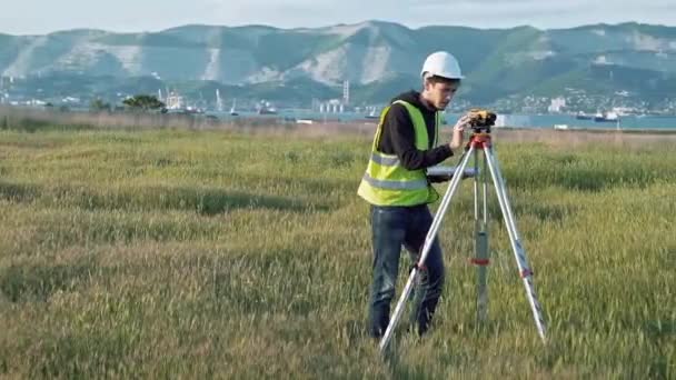 İş elbiseleri içinde erkek bir surveyor ekipman inşaat alanı üzerinde ayarlar. Peyzaj konsept tasarımı, Jeodezi — Stok video