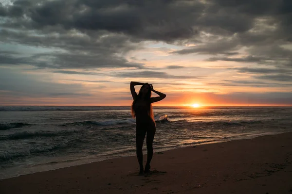 Frontansicht Silhouette einer attraktiven Frau. schönes junges Mädchen mit langen Haaren, das am Strand spaziert und bei Sonnenuntergang posiert. Konzept des Reisens, der Entspannung, des Yoga — Stockfoto