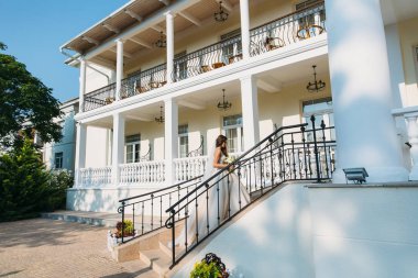 Zarif gelin düğün çiçek kokulu, gelinlik çekici kadın. Beyaz elbiseli genç kız güzel beyaz bir ev merdiven gider. Mutlu yeni evli bir kadın. Gelin düğün makyaj ile