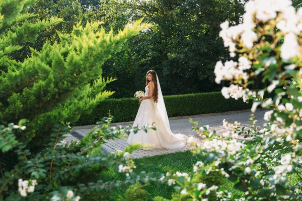 Menina em um vestido branco no prado. Mulher em um belo vestido longo posando no jardim. Noiva deslumbrante em um vestido de noiva — Fotografia de Stock