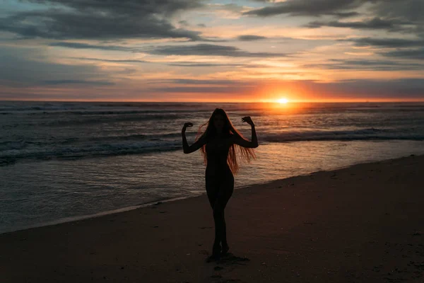 Frontansicht Silhouette einer attraktiven Frau. schönes junges Mädchen mit langen Haaren, das am Strand spaziert und bei Sonnenuntergang posiert. Konzept des Reisens, der Entspannung, des Yoga — Stockfoto