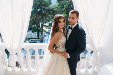 birbirlerine kucaklayan ve beyaz bir Balkonda duran güzel çift balayı. Elele bir gelinlik uzun saçlı genç siyah bir takım elbise ve çok güzel bir gelin damat.