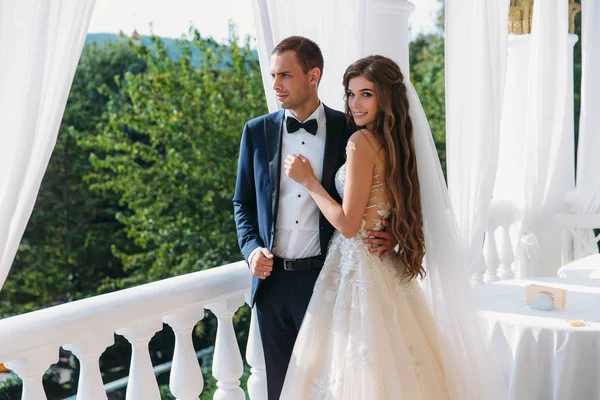 Schöne Braut mit langen Haaren in weißem Kleid umarmt Bräutigam und lächelt niedlich. charmantes Paar Hochzeitspaar am Hochzeitstag. eine glückliche Familie im Hotelzimmer. — Stockfoto