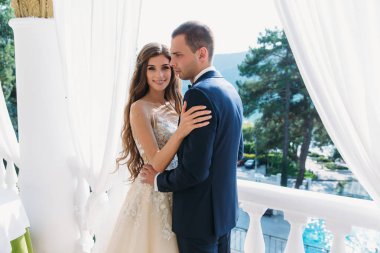 birbirlerine kucaklayan ve beyaz bir Balkonda duran güzel çift balayı. Elele bir gelinlik uzun saçlı genç siyah bir takım elbise ve çok güzel bir gelin damat.