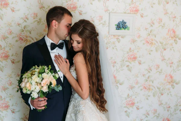 Schöne Braut mit langen Haaren in weißem Kleid umarmt Bräutigam und lächelt niedlich. charmantes Paar Hochzeitspaar am Hochzeitstag. eine glückliche Familie. — Stockfoto