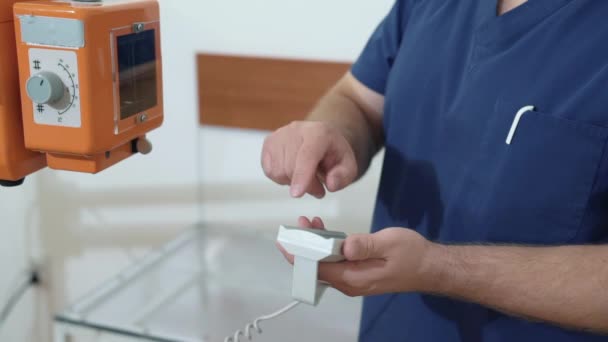 A male doctor adjusts the X-ray machine using a remote control. Close up mans hands in medical clothes with medical equipment. Concept of health, work in the hospital. — Stock Video