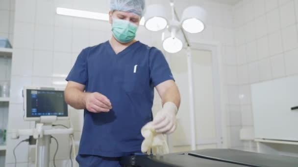 Adult doctor in professional clothes with a mask on his face wearing medical gloves. Sterile gloves on the hands of a surgeon, medical tools in a hospital. — Stock Video