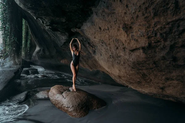 Девушка в черном купальнике позирует на пляже с вулканическим песком. Модель с сексуальным телом покоится на море . — стоковое фото