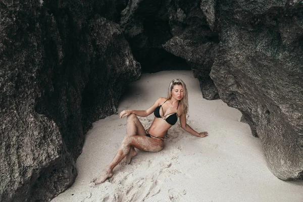 Сексуальная молодая девушка в черном купальнике позирует на пляже. Красивая блондинка с длинными волосами отдыхает у океана. Концепция спортивной модели, купальников — стоковое фото