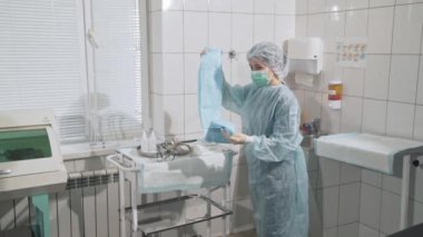 Tıp aletleri, sağlık, hastane kavramı. Bir doktor steril giyim üzerine koymak bir kadın hemşire yardımcı olur. Uzmanlar timinin profesyonel eseri. Klinikte ekipman..