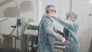 Tıp aletleri, sağlık, hastane kavramı. Bir doktor steril giyim üzerine koymak bir kadın hemşire yardımcı olur. Uzmanlar timinin profesyonel eseri. Klinikte ekipman..