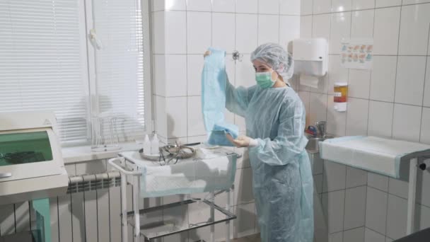 Tıp aletleri, sağlık, hastane kavramı. Bir doktor steril giyim üzerine koymak bir kadın hemşire yardımcı olur. Uzmanlar timinin profesyonel eseri. Klinikte ekipman.. — Stok video