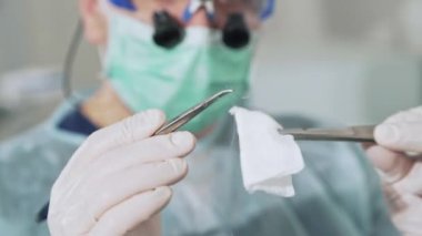 Portre, cerrah cerrahi iğne elinde, gözlüklü arka planda bir doktor ile bir kelepçe tutar. Hastanede steril belgesine bakın. Önce tıbbi malzeme hazırlanması