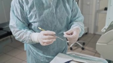 Portre, cerrah cerrahi iğne elinde, gözlüklü arka planda bir doktor ile bir kelepçe tutar. Hastanede steril belgesine bakın. Önce tıbbi malzeme hazırlanması
