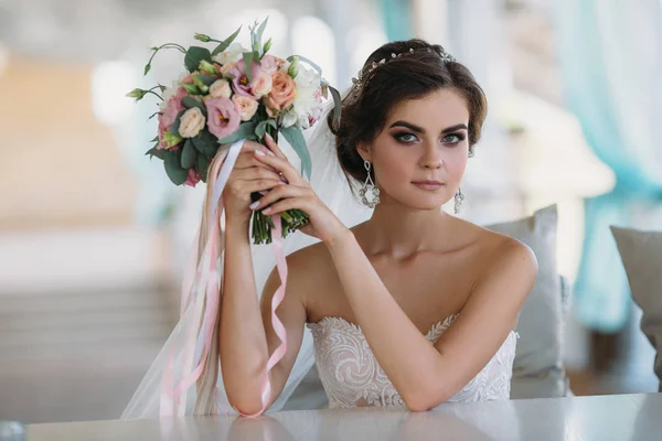 Jovem noiva bonita morena em vestido branco com bela maquiagem, penteado e buquê de flores. Conceito de casamento. Mulher de beleza incrível retrato . — Fotografia de Stock