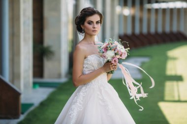 Güzel makyaj, saç modeli ve buket çiçek beyaz elbiseli genç güzel esmer gelin. Evlilik kavramı. Şaşırtıcı güzellik kadın portre.