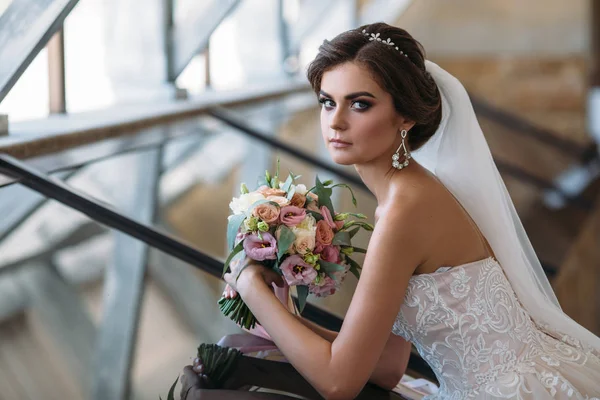 Porträt einer schönen Braut mit Blumenstrauß im weißen Luxuskleid. hinreißende Modell mit Braut-Make-up und Frisur mit einem Diadem im Haar, Diamant-Ohrringe im Ohr. Heirat und Floristik — Stockfoto