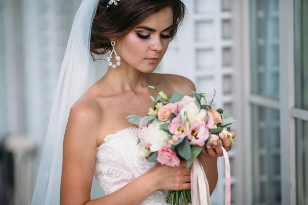 Retrato de noiva bonita com flores de buquê em vestido de luxo branco. Modelo lindo com maquiagem nupcial e penteado com um diadema em seu cabelo, brincos de diamante no ouvido. Casamento e florística — Fotografia de Stock