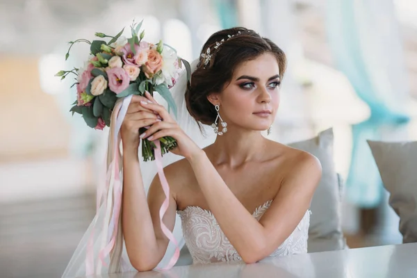 Porträt einer schönen Braut mit Blumenstrauß im weißen Luxuskleid. hinreißende Modell mit Braut-Make-up und Frisur mit einem Diadem im Haar, Diamant-Ohrringe im Ohr. Heirat und Floristik — Stockfoto
