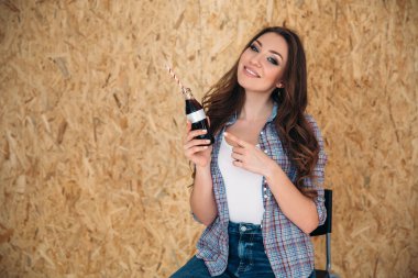 Bir şişe içki ile gösterilen bir gülümseyen kız portresi. Güzel bir genç kadın bir makyaj ve bir lüks saç modeli ile ekose gömlekli su onun elinde tutar. Boşaltmak için logo yazıt